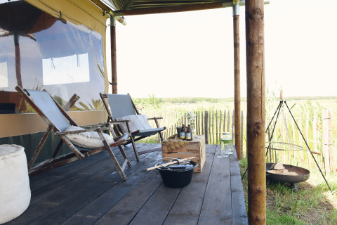 Glamping en Duynpark Het Zwanenwater Woodlodges, Holanda del Norte, con terraza, sillas y fogata.