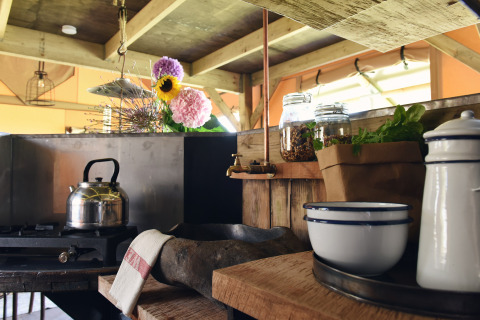 Cuisine rustique de glamping aux Woodlodges Noord-Holland avec bouilloire, bocaux, herbes et fleurs.