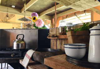 Rustieke glampingkeuken bij Woodlodges Noord-Holland met waterkoker, kruiden, potten en verse bloemen.