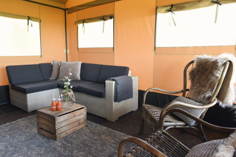 Gezellige zithoek in een luxe tent bij Duynpark Het Zwanenwater Woodlodges Noord-Holland met houten meubels.