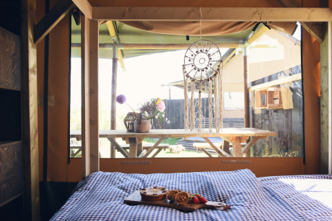 Interior view of glamping wood lodge with bed, breakfast, and dreamcatcher at Duynpark Het Zwanenwater.