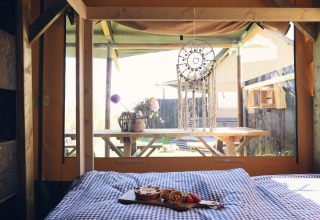 Interno di una lodge in legno glamping con letto, colazione e acchiappasogni a Duynpark Het Zwanenwater.