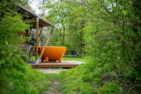 Glamping bij Erfgoed Bossem met een groot oranje buitenbad omringd door weelderige groene natuur en bos.