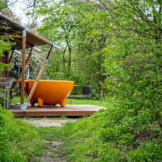Glamping all'Erfgoed Bossem con grande vasca da bagno arancione all'aperto immersa nel verde rigoglioso.