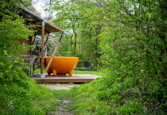 Glamping-Unterkunft bei Erfgoed Bossem mit orangefarbener Outdoor-Badewanne in grüner Naturumgebung.