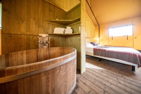 Interno di una tenda glamping a Erfgoed Bossem Lodgetenten Twente con vasca in legno, letto e scaffali.