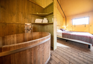 Indretning af glamping-telt på Erfgoed Bossem Lodgetenten Twente med trægulv, badekar og dobbeltseng.