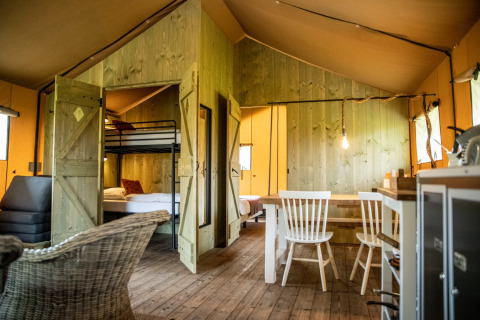 Indretning af glamping-indkvartering i Erfgoed Bossem Lodgetenten Twente med rustikke træmøbler.