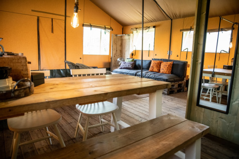 Interno accogliente di glamping presso Erfgoed Bossem - Lodgetenten Twente con mobili in legno e divano.