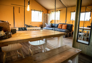 Hébergement glamping à Erfgoed Bossem - Lodgetenten Twente avec meubles en bois rustiques et canapé confortable.
