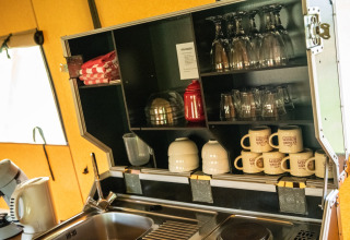 Keukenruimte in Erfgoed Bossem lodgetent in Twente met kopjes, glazen, handdoeken en wasbak.