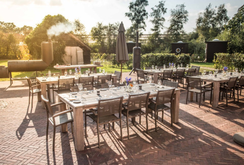 Outdoor dining area with wooden tables and chairs at Erfgoed Bossem - Lodgetenten Twente glamping site.
