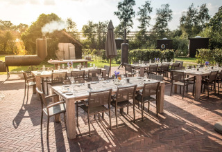 Zona de comedor al aire libre con mesas y sillas de madera en Erfgoed Bossem - Lodgetenten Twente glamping.