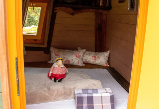 Binnenzicht van de Boomhut-glamping bij Dierentuin Schwerin met kussens, pop en houten venster.