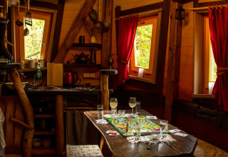 Gezellig boomhutinterieur van Boomhut - Dierentuin Schwerin met houten tafel, bordspel en rode gordijnen.