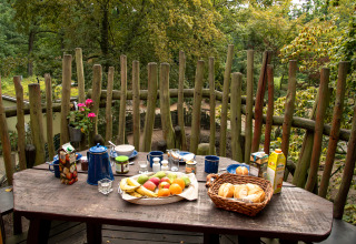 Desayuno al aire libre en el balcón casa del árbol en Zoo Schwerin con pan, fruta, jugo y vista al bosque.
