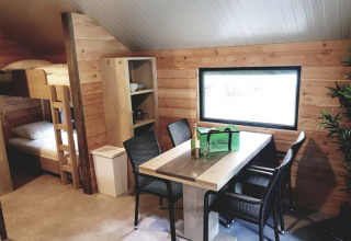 Vista interna di un alloggio glamping presso Camping Alf - Chalets Rijnland-Palts con letti a castello e tavolo da pranzo.