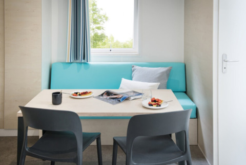 Comedor en Camping Alf - Chalets Renania-Palatinado con banco azul, sillas grises y desayuno en la mesa.