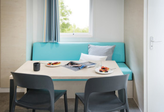 Coin repas aux Chalets Camping Alf - Rhénanie-Palatinat avec banc bleu, chaises grises et petit-déjeuner.