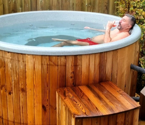 Hombre relajándose en un jacuzzi de madera en Camping Alf - Chalets Rijnland-Palts, al aire libre.