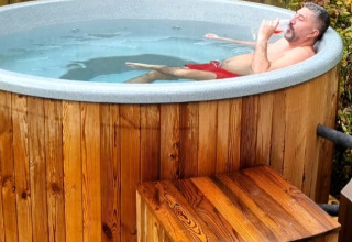 Uomo che si rilassa in una vasca idromassaggio di legno al Camping Alf - Chalets Rijnland-Palts.