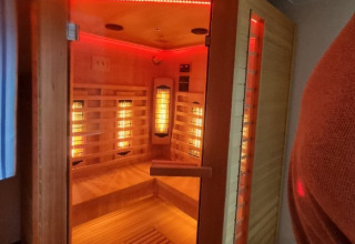 Sauna de infrarrojos moderna con bancos de madera y luces LED rojas en Camping Alf - Chalets Rijnland-Palts.