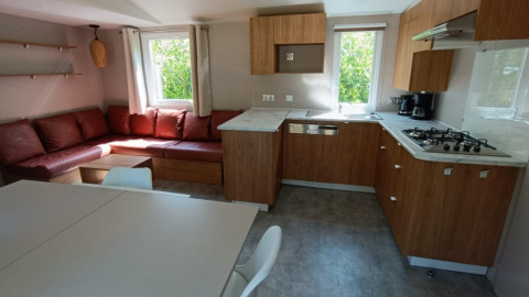 Modern glamping accommodation with wooden kitchen, corner sofa and large windows at Camping Alf - Chalets Rijnland-Palts.