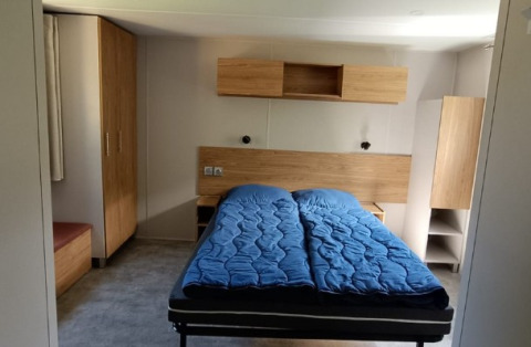 Innenansicht eines Glamping-Chalets bei Camping Alf - Chalets Rijnland-Pfalz mit Doppelbett und Holzmöbeln.