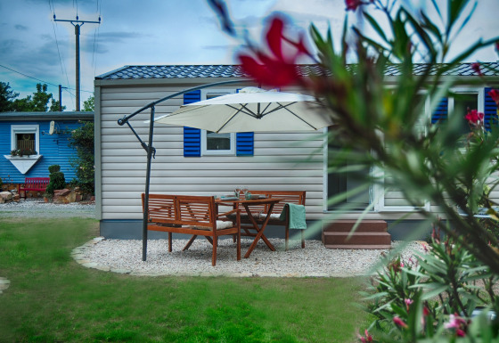 Buitenruimte met houten tafel, stoelen en parasol bij luxe stacaravan op Camping Nahemühle, Rijnland-Palts.