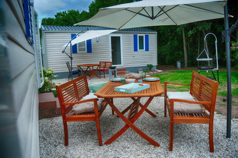 Coin repas extérieur avec table et bancs en bois sous parasol devant mobil-home de luxe Camping Nahemühle.