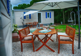 Área exterior con mesa y bancos de madera y parasol junto a caravana de lujo en Camping Nahemühle.