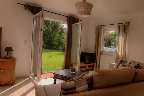 Salon de glamping luxueux au Camping Nahemühle avec portes ouvertes sur jardin vert et canapé confortable.