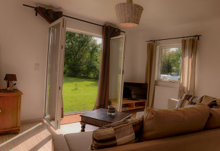 Luxe glamping woonkamer bij Camping Nahemühle met open deuren naar groene tuin en comfortabele bank.