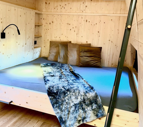 Premium-Chalet-Schlafbereich mit Holzverkleidung, Doppelbett und Kissen bei Alpencamping Nenzing in Vorarlberg.