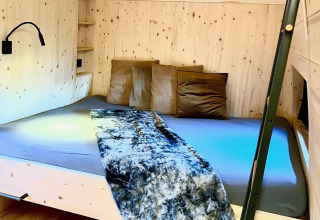 Camera da letto chalet premium con pareti in legno, letto matrimoniale e cuscini ad Alpencamping Nenzing, Vorarlberg.