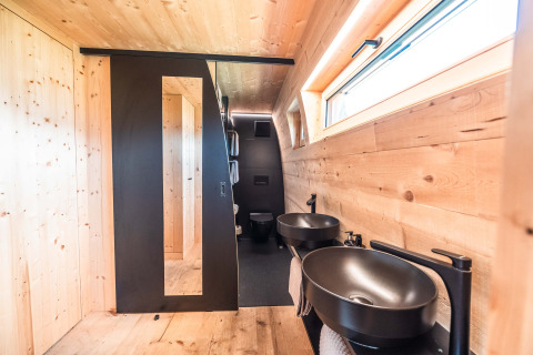 Modern bathroom with wooden walls and black fixtures in Alpencamping Nenzing's premium chalet, Vorarlberg.