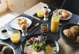 Genuss am Frühstückstisch mit Brötchen, Gebäck, Eiern und Saft im Alpencamping Nenzing Premium Chalet in Vorarlberg.