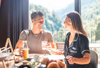 Coppia che fa colazione nello chalet glamping soleggiato di Alpencamping Nenzing, in Vorarlberg.