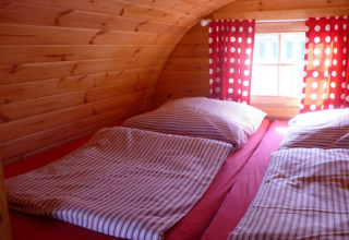 Interior of glamping accommodation with wooden walls, two single beds, striped bedding, and red polka dot curtains.