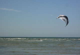 Person kite surfing on shallow sea near Camping Ostseequelle-Wijnvaten Ostzee, Germany, under a blue sky.