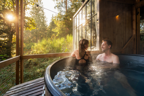 Ein Paar genießt einen entspannten Moment im Outdoor-Whirlpool der Nutchel Cabins - Tiny Houses Elzas im Wald.