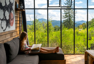 A girl reads a book on a sofa inside a Nutchel Cabin, with large windows showing scenic mountain views.