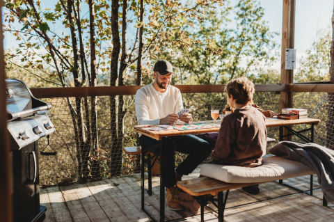 Padre e hijo juegan cartas en la terraza de Nutchel Cabins - Tiny Houses Elzas, rodeados de naturaleza.
