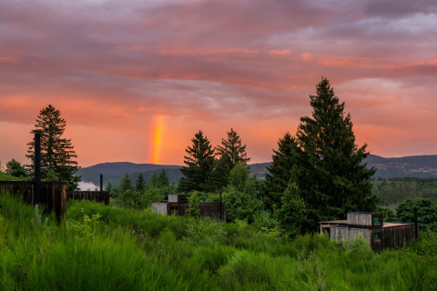Nutchel Cabins Tiny Houses Elzas i en frodig skov med solnedgang og regnbue på himlen, glamping oplevelse.