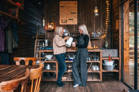 Due donne si godono un momento in una cucina rustica di legno presso Nutchel Cabins - Tiny Houses Elzas per glamping.