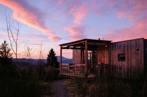 Nutchel Cabins - Tiny Houses Elzas glamping cabin at sunset, wooden tiny house in a forest setting, colorful sky.