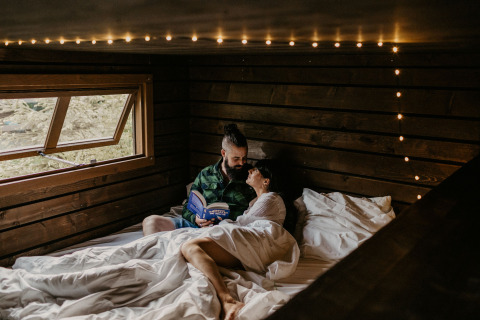 Paar entspannt im Bett mit Buch in Nutchel Cabins - Tiny Houses Elzas, gemütliche Glamping-Unterkunft.