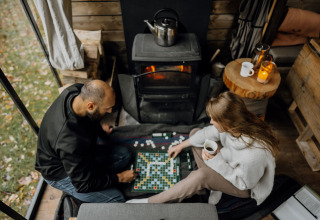 Coppia che gioca a un gioco da tavolo davanti alla stufa in una cabina di Nutchel Cabins - Tiny Houses Elzas.