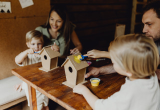 Famille peignant des nichoirs à une table dans Nutchel Cabins - Tiny Houses Elzas pendant un séjour glamping.