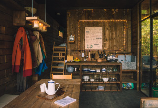 Gezellige houten Nutchel Cabin met open keuken, eethoek, jassen en uitzicht op het bos door grote ramen.